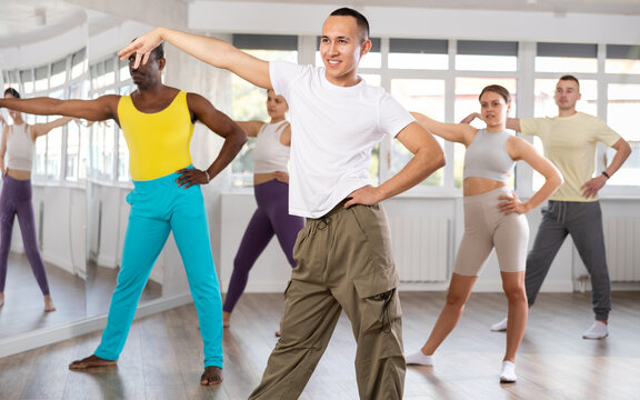 European guy teaches sequences of movements, actions during dance lesson, trains to doing elements of dancehall dance, enjoys active hobby. Multinational group rehearsal, dance choreography coach
