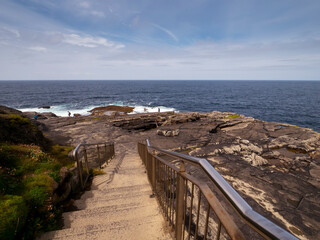 Obraz premium Stairs on rough stone coast and blue ocean and cloudy sky. Nature scene in Kilkee area, county Clare, Ireland. Popular travel area with amazing nature scenery.
