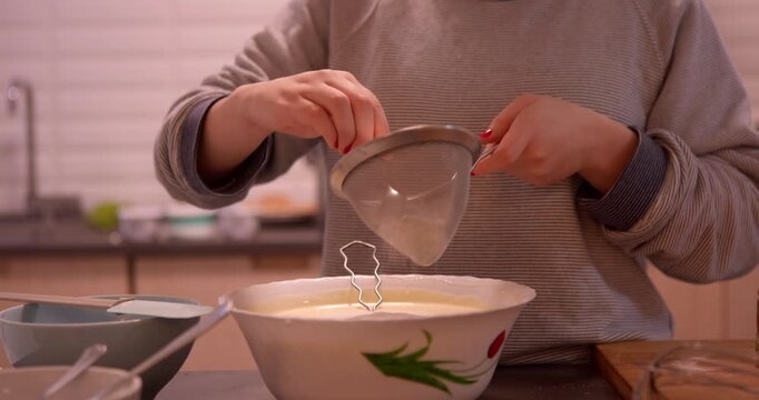 Sifting the Flour: Hands carefully sift flour into a mixing bowl, preparing for a culinary endeavor in a domestic kitchen setting.