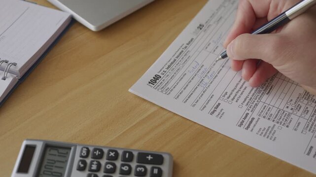 Man Filling In The Tax Form 1040. Person Calculates of Planning Budgets Yearly Personal Finance and Fills up US Tax Form 1040. Signing 1040 Income Tax Return. Names and numbers are fictitious.