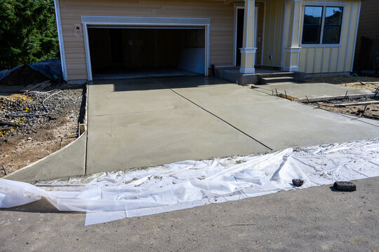 New home construction, housing supply, freshly poured wet concrete driveway and front patio, sunny day on new neighborhood development winter job site
