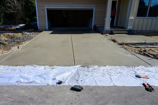 New home construction, housing supply, freshly poured wet concrete driveway and front patio, sunny day on new neighborhood development winter job site
