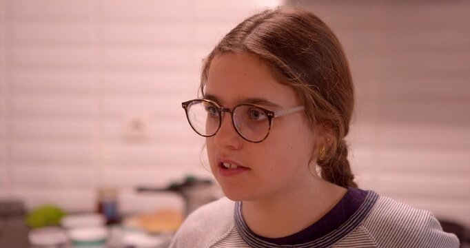 Young person with glasses focused, indoors: A young individual with glasses, focused and contemplative, indoors, in a home environment.