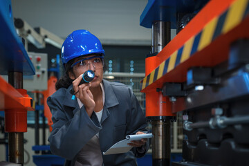 Indian female industrial engineer checks machinery with a flashlight while performing quality...