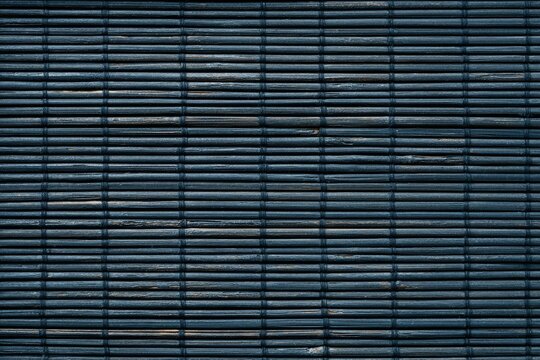 A close-up of a tightly woven, textured blue-gray blind with horizontal bamboo slats