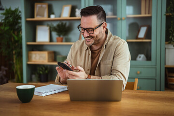 Happy man using smart phone while working remotely from home