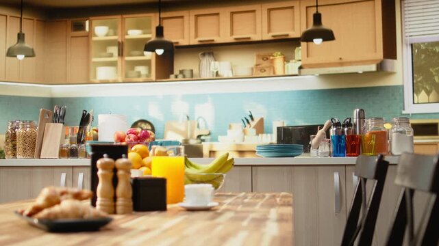 Kitchen with wooden breakfast table with pastry and fruits in empty home, natural light enhances rustic design, showing kitchenware and utensils. Decorative items in spacious room with no people.