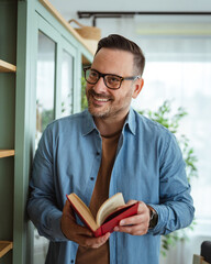 Happy man in glasses reading book at home