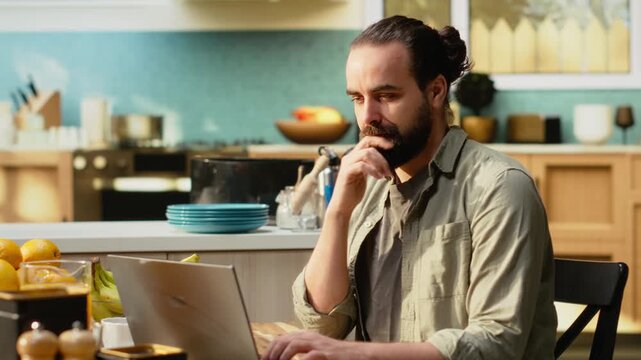 Portrait of adult man working from home in cozy rustic kitchen, using laptop for daily tasks online. Freelancer lifestyle with remote work setup supporting productivity and multitasking.
