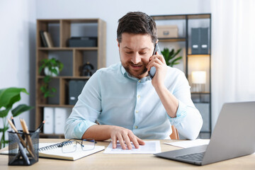 Naklejka premium Man talking on smartphone at wooden desk indoors