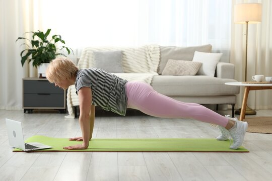 Senior woman practicing yoga via video chat with online coach at home. Fitness and sport