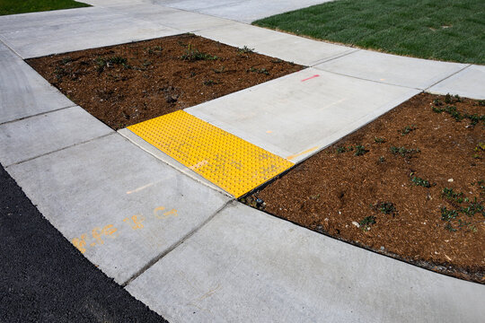 Freshly installed concrete sidewalk, yellow ADA Curb Ramp, and landscaping in new residential neighborhood development on sunny winter day
