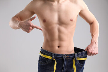 Athletic man wearing big jeans with measuring tape on light grey background, closeup
