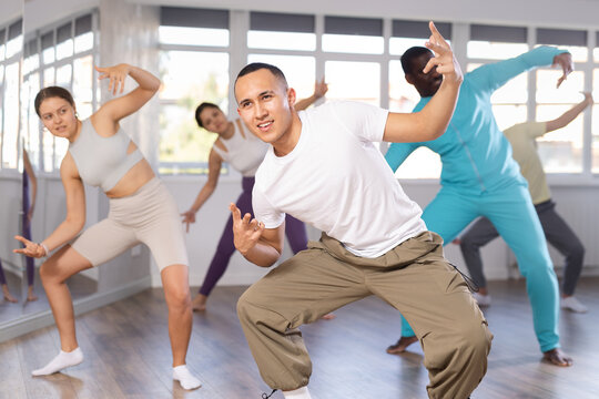 Cheerful young Asian man practicing modern street dancing during group class in choreographic studio..
