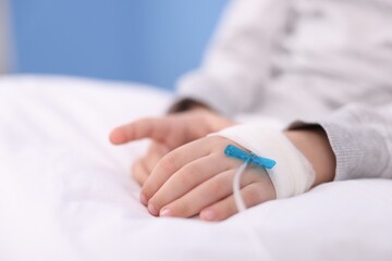 Fototapeta premium Little child with IV drip on bed in hospital, closeup. Space for text