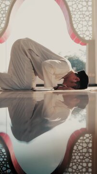 A Muslim man performing Islamic pray inside a mosque during Ramadan, a peaceful spiritual moment with beautiful mosque architecture and reflection on the polished floor.