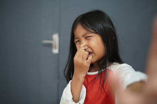Disgusted little Asian girl pinching her nose due to bad smell, child reacting to unpleasant odor or stinky scent with funny expression, air pollution