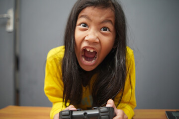 Frustrated little Asian girl grimacing while playing video games, upset child losing a game holding...