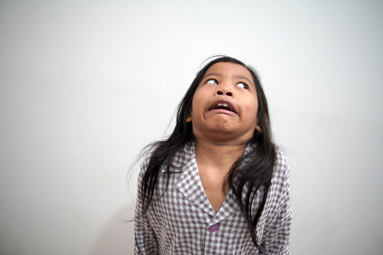 Funny Asian little girl making a mocking and teasing face expression. Portrait of cute expressive kid with silly facial grimace. Childhood humor, naughty behavior, and comical reaction concept