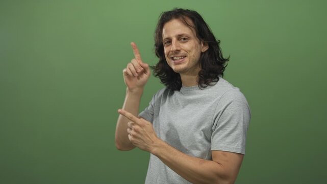 Man points finger upward with both hands and smiles in studio against green wall; friendly helpful tip.