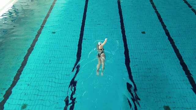 Professional swimmer training backstroke technique in a blue swimming pool with lanes, high angle view
