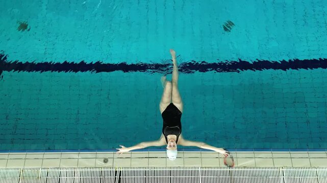 Professional female swimmer floating and relaxing in a blue pool after a hard training session. High angle view