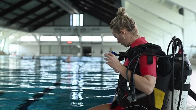 Female scuba diver preparing her equipment sitting on the edge of a swimming pool for a diving lesson in wetsuit