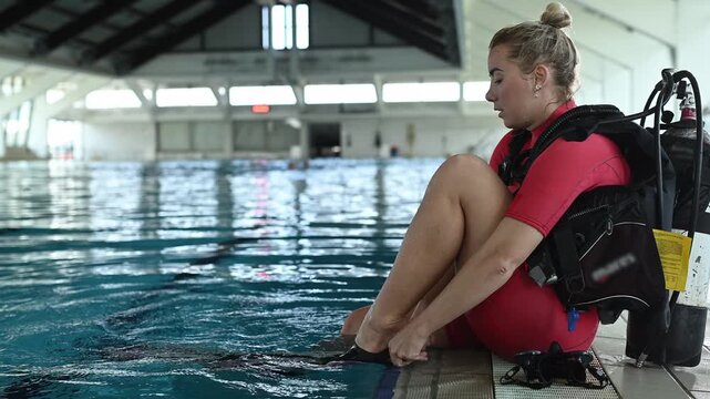 Woman diver preparing for a dive, putting on fins and mask at the poolside before showing the ok sign