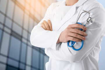 Naklejka premium Doctor holding stethoscope against hospital outdoors, closeup. Space for text