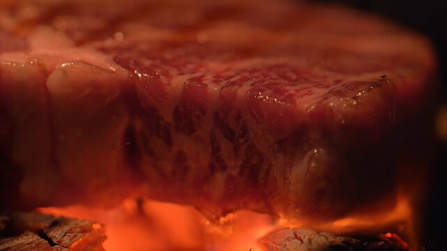 Grilled steak sizzles on hot coals at night