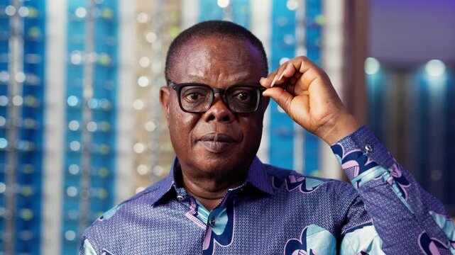 Elder African man wearing glasses, looking confidently at the camera with bokeh lights background in eyewear shop