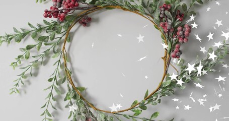 Displaying wreath adorned with green sprigs, frosted red berries and white stars on pale gray table