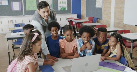 Leaning teacher wearing sweater guiding students in classroom, with open laptop and pencil case