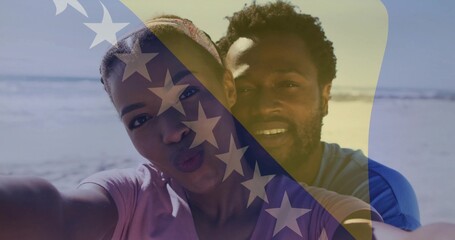 Naklejka premium Posing couple wearing T-shirts, puckering lips while leaning in for selfie at beach, flag overlay