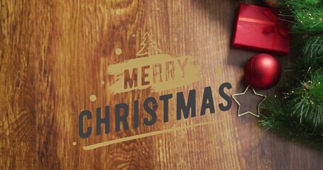 Displaying MERRY CHRISTMAS text on wood tabletop, showing red box and bauble, gold star, pine sprig © vectorfusionart