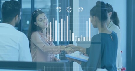 Presenting four staff in business casual gesturing toward projected chart on office glass, tablet