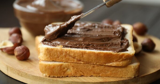 Woman spreading chocolate paste onto toast at table, closeup
