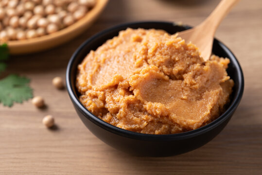 Traditional Japanese miso paste in a black bowl with spoon on a rustic wooden table. Healthy fermented soybean seasoning for cooking