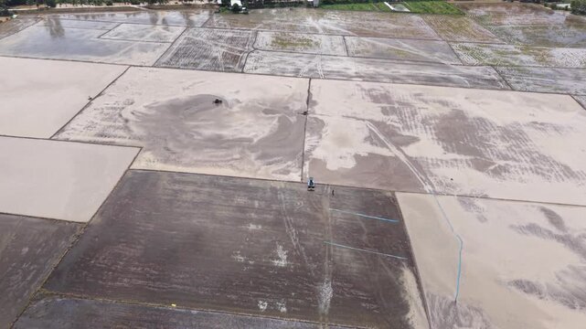 Aerial drone view of tractor leveling muddy rice field during farming season in Vietnam