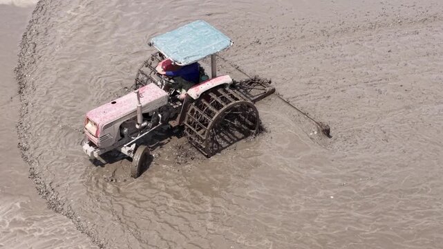 Aerial drone view of tractor leveling muddy rice field during farming season in Vietnam