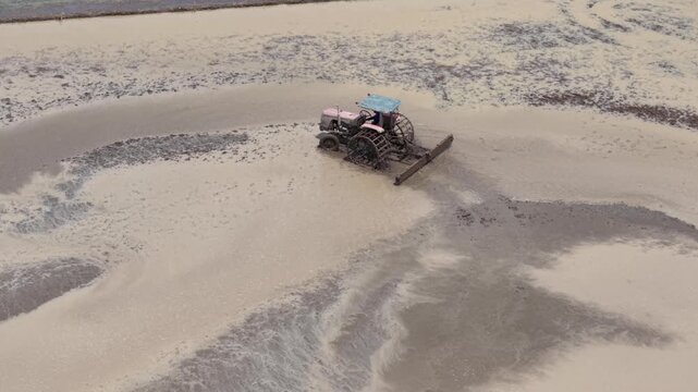 Aerial drone view of tractor leveling muddy rice field during farming season in Vietnam