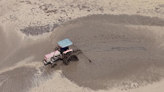 Aerial drone view of tractor leveling muddy rice field during farming season in Vietnam