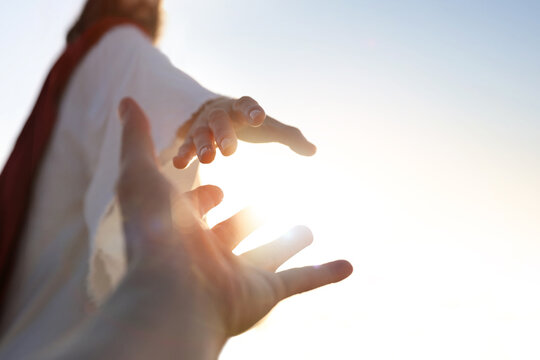 A desperate Christian hand reaching out to the hand of Jesus Christ, with a bright sunny background, concept of faith and salvation.
