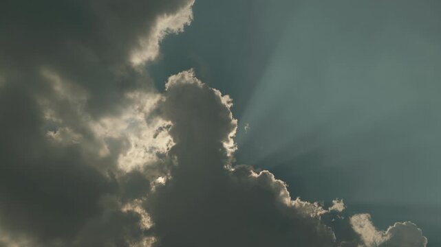 Cinematic stock footage of crepuscular rays (God rays) piercing through heavy, moving dark clouds. The shot captures the dynamic movement of the sky with bright sunlight.