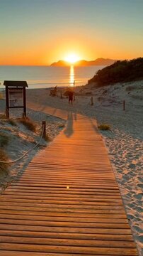 Cinematic 4K vertical sunrise on a Mediterranean beach in Mallorca, with a wooden boardwalk through sand dunes leading to turquoise sea and distant mountains in warm morning light.
