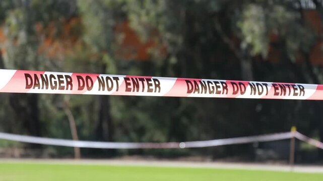 Danger do not enter warning tape fluttering in the wind marking a restricted area outdoors. Safety barrier cordon used to block access and warn people of potential hazards.
