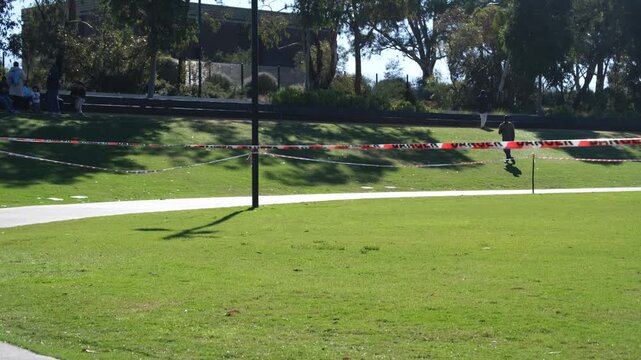 Safety barrier tape cordoning off an area in a public park in Australia. Warning tape around green lawn and pedestrian path marking a restricted zone for maintenance in an outdoor recreational space