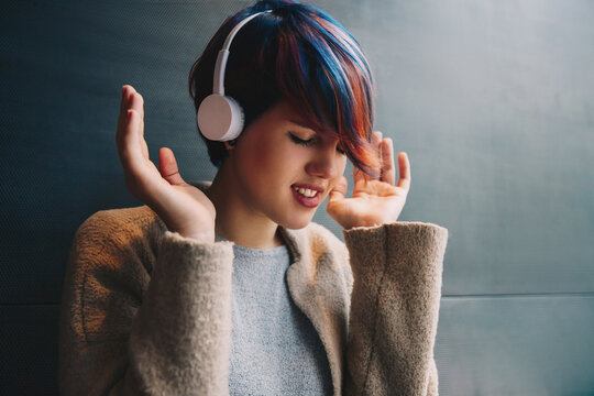 Mental care. Rest. Technologies. Listening to music. Young woman with short colorful haircut in headphones is enjoying, her eyes are closed