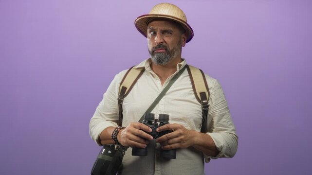 Man holding binoculars with hands against purple backdrop in studio; curiosity travel exploration adventure.