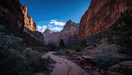 Sunlit red rock canyon trail leading toward distant jagged peaks under blue sky